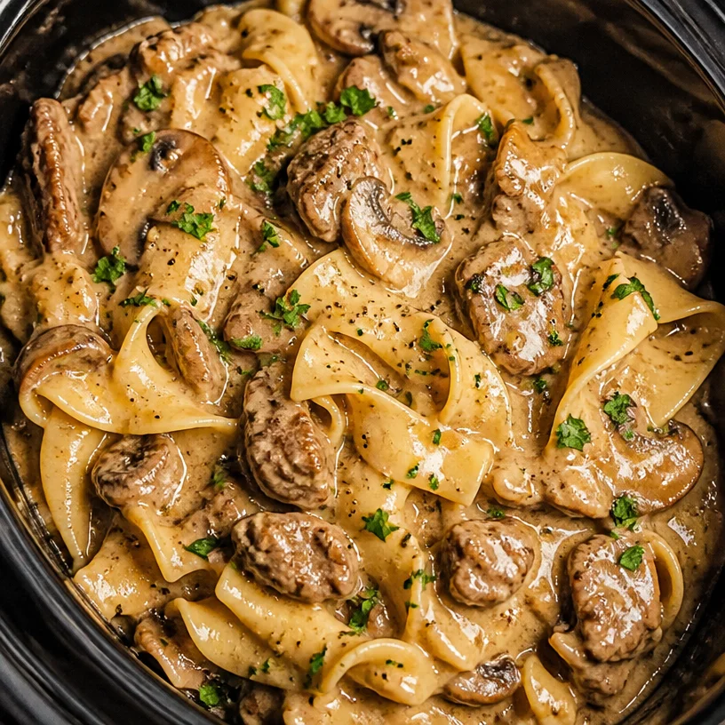 Crock Pot Beef Stroganoff served in a bowl with noodles and garnished with parsley